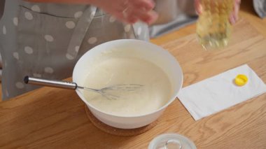 Bir kadın şişeden yeni yapılmış bir hamura sebze yağı dökerek nemli bir doku için yağ ekler. Krep ya da waffle tarifi malzemelerini karıştırmak için karışımı çırpıyor..