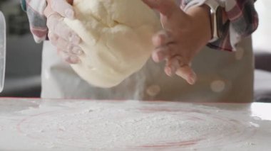 The process of making homemade bread. A cook's hands sprinkle flour on a work surface and knead raw elastic dough. A culinary hobby and the preparation of ingredients for a delicious meal.
