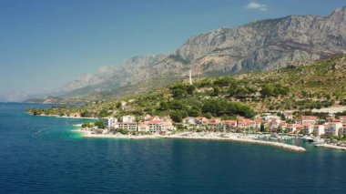 A beautiful travel destination on the Croatian Riviera. This scenic aerial view shows the town of Podgora, its boat harbor, and the majestic mountains meeting the clear Adriatic Sea.