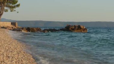 Turquoise waves of the Adriatic sea wash over a beautiful pebble beach in Podgora, Croatia. A picturesque and idyllic summer vacation destination on the famous Makarska Riviera coast.