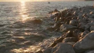 The sun glitters on the Adriatic sea during a beautiful Croatian sunset. A small boat floats near a rocky breakwater, a perfect summer holiday and travel destination on the Makarska Riviera.