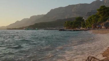 A beautiful pebble beach on the Makarska Riviera with the Biokovo mountains rising above the resort town of Podgora, Croatia. A perfect summer holiday destination with clear Adriatic sea water.