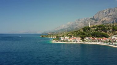A beautiful beach on the Adriatic coast of Croatia, with tourists swimming and sunbathing in the clear turquoise sea. A perfect summer holiday scene on the picturesque Podgora Riviera.