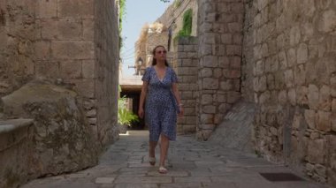 A woman on a city tour walks through a medieval alley looking at old buildings in Korcula. Sightseeing and travel to a European destination with ancient architecture and cultural heritage.