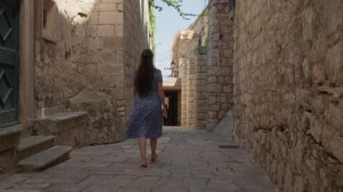 Rear view of a female traveler exploring an ancient city on a summer vacation in Korcula. Solo journey and wanderlust concept for discovering the historic stone passages of an old Croatian town.