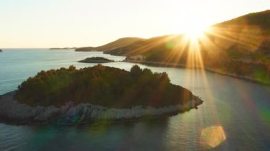 A stunning island on the Croatian coast filmed by a drone during a scenic sunset. The warm golden hour light creates beautiful sun flares over the calm Adriatic Sea. A truly cinematic travel shot.