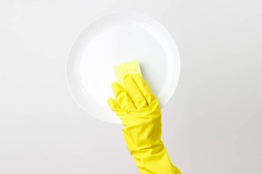 Eldivenli biri beyaz arka planda bir tabak yıkıyor.