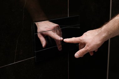 close-up of a man pressing the chrome button to flush the toilet in the bathroom
