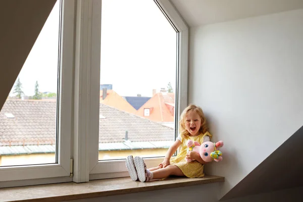 Stock image Little Girl Smiling with a Soft Toy on a Cozy Window Seat