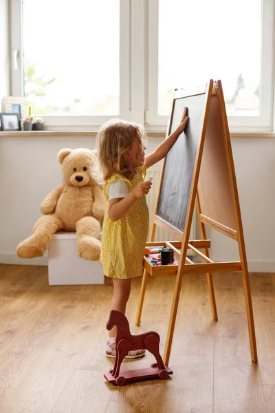 Küçük Kız Evdeki Bir Çocuk Odasında Tebeşirle Tahtaya Resim Çiziyor — Stok fotoğraf