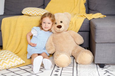 Evinde kocaman yumuşak bir oyuncak ayıyla küçük bir kız.