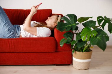 Kadın kanepede uzanıyor ve akıllı telefon kullanıyor.