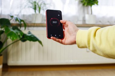 Elinde akıllı bir telefondan iklim kontrol uygulaması arayüzü. Basit sıcaklık kontrolü ve otomatik ısıtma kavramı.