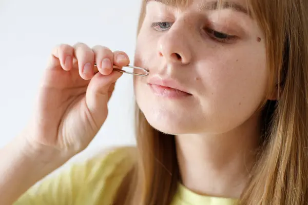 woman plucking hair above her upper lip with tweezers