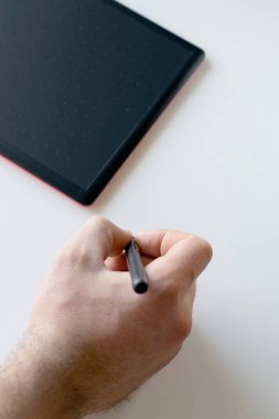 Klasik dikdörtgen grafik tableti. Tasarım, rötuş ve grafikler için beyaz bir masada yatan bir adam tarafından tutulan bir kalem.