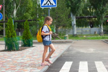 6-8 yaşlarında uzun sarı saçlı bir kız öğrenci okula giderken karşıdan karşıya geçiyor. Zebra geçiyor. Yaya geçidinden geçen yayaların güvenliği kavramı..