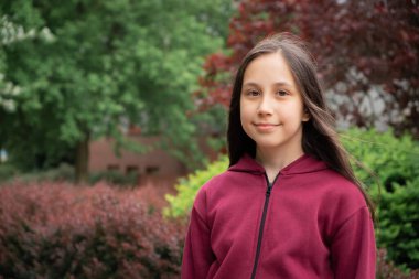 10-11 yaşındaki neşeli esmer bir kızın portresi. Uzun saçlı. Sokakta kırmızı yeşil yapraklar var..