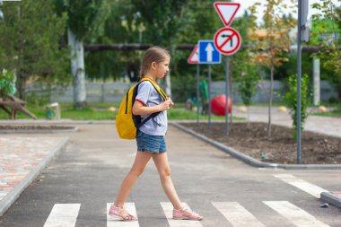 6-8 yaşlarında uzun sarı saçlı bir kız öğrenci okula giderken karşıdan karşıya geçiyor. Zebra geçiyor. Yaya geçidinden geçen yayaların güvenliği kavramı..
