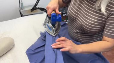 Bir kadın terzi elbisenin yan dikişlerini düzleştiriyor. Bir moda uzmanı, bir moda fabrikası veya stüdyo, bir atölye, bir tasarım girişimi vizyonu.