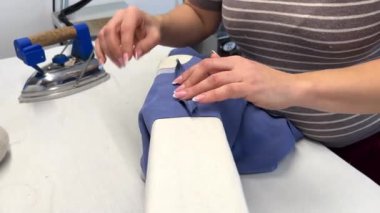 Bir kadın terzi bir elbisenin omuz dikişlerini ütülüyor. Moda alanında bir uzman, bir moda fabrikası veya stüdyo, bir atölye, bir tasarım girişimi vizyonu.