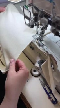 Dikiş işlemi. Bir terzi, ürünün örülmüş kumaş ve işleme bölümünü kapaklı üç iğne ve bir motorla birlikte endüstriyel dikiş makinesine kurdele ile diker. Dikey video