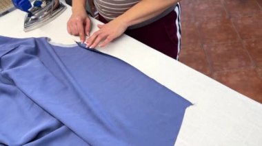 Kadın bir terzi ütü masasında bir elbiseyi ütülemek için çalışıyor. Bir moda uzmanı, bir moda fabrikası veya stüdyo, bir atölye, bir tasarım girişimi vizyonu.