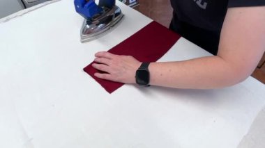 Pantolon dikme süreci. El ütü masasının beyaz yüzeyinde, pantolonun kırmızı kısmındaki demire basar..