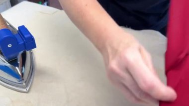 Pantolon dikme süreci. Bir el buharlı ütüyle kırmızı kumaş bir elbiseye dikiş atar. Kırmızı Kumaş Elbiseye Dikiş Basmak