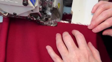 Serger makinesinde kırmızı kumaş parçasına rehberlik eden ellerin yakın görüntüsü. makine kesiğin kenarını işlerken temiz ve profesyonel bir son kumaş oluşturur kendi üzerine katlanır.