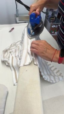 Etkili teknikler ve beceriler sergileyen çizgili bir gömleğin nasıl ütüleneceğini gösteren bir kişi. Bireyler kumaşı dikkatlice ütü masasına yerleştirir, buhar ütüsüyle kırışıklıkları temizler..