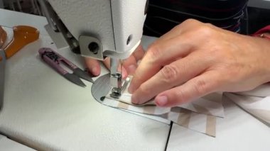 Bir el, beyaz endüstriyel dikiş makinesinin iğne deliğinden geçirilmiş kumaşa dikkatle rehberlik eder. Endüstriyel dikiş makinesine dikiş atmanın karmaşık sürecini yakından gözlemliyorum.