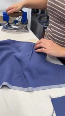 Bir kadın terzi elbise diker ve ütüler. Moda alanında bir uzman, bir moda fabrikası veya stüdyo, bir atölye, bir tasarım girişimi vizyonu. Dikey video.