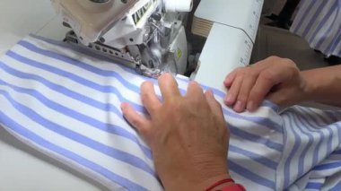 Dikiş işlemi. El, mavi ve beyaz çizgili kumaşı yavaşça sanayi kapısından geçirir. Endüstriyel dikiş makinesindeki karmaşık dikiş işlemini dikkatle izleyin..
