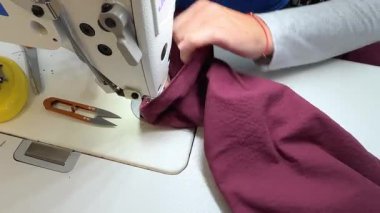 Tekstil işçisi profesyonel giysiler yapmak için dikiş makinesi kullanıyor. Moda üretiminde hassasiyet. Endüstriyel dikiş makinesine dikiş atmanın karmaşık sürecini yakından gözlemliyorum..