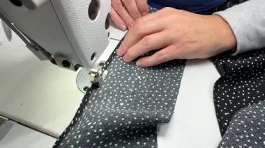 Elbise dikme süreci. Benekli kumaşı diken bir dikiş makinesinin yakın çekimi. Bir terzi malzemeye dikkatle rehberlik eder. Süreç zanaatkarlığı ve ayrıntılara dikkati vurguluyor.