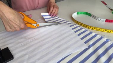 Atölyede kıyafet yaratma süreci. Terzi mavi çizgili kumaşı büyük bir makasla dikkatlice kesiyor. Dikiş deseninin rehberliğinde. Tekstil üretimi ve terziliğin ayrıntılı bir görünümü.