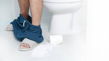 Diarrhea. Man sitting up close on the toilet bowl on a white background. clipart