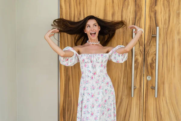 Young beautiful woman in a romantic dress with a floral print, and a pearl necklace bracelet, against the background of a wooden door, laughs smiles has fun