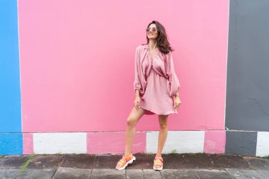 Young beautiful smiling cute romantic woman in trendy summer dress. Carefree woman posing in the street near pink wall. Positive model outdoors in sunglasses. Cheerful and happy.