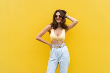 Young beautiful woman. Carefree woman posing in the street near yellow wall. Positive model outdoors in sunglasses. Happy and cheerful