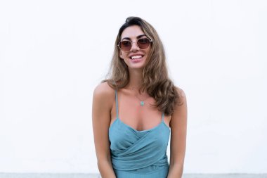 Portrait of beautiful woman in green fitting summer dress on white background natural day light, wearing sunglasses, smiling excited
