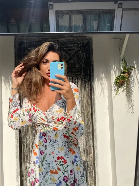 女性で夏のドレスで花春のプリントで自宅屋外で写真を撮る携帯電話でミラー用ソーシャルメディア — ストック写真