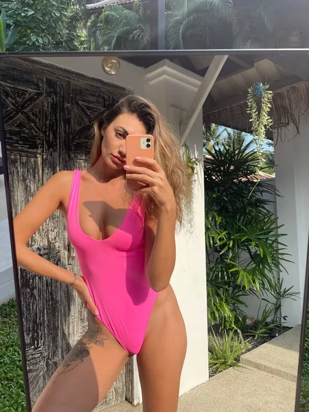 在户外 穿着亮晶晶粉色泳衣的体态丰满的晒得发亮的女人在手机上拍照 在社交媒体 垂直的镜子中拍照 — 图库照片