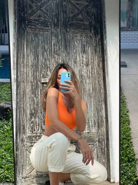 フィット日焼けした女性でオレンジトップと居心地の良い快適なパンツに自宅屋外で写真を撮る自撮りで電話でミラー用ソーシャルメディア — ストック写真