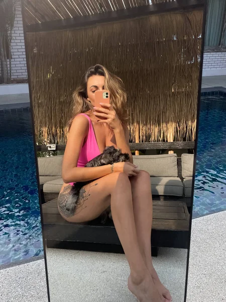 フィットスポーティな日焼けした女性で明るいピンクの水着屋外でホーム取る写真自撮りで電話でミラー用ソーシャルメディア 垂直プールによって子犬 — ストック写真