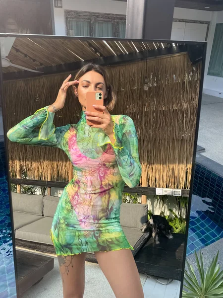 在户外 穿着绿色的短而透明的长裙 穿着运动健美的晒黑了的女人在户外的社交媒体的镜子里拍照 垂直地在游泳池边拍摄 — 图库照片
