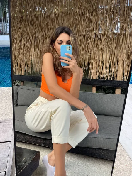 在户外 穿着橙色上衣和舒适舒适的裤子的晒黑的女人在手机上拍照 在镜子里为社交媒体 垂直拍摄 — 图库照片
