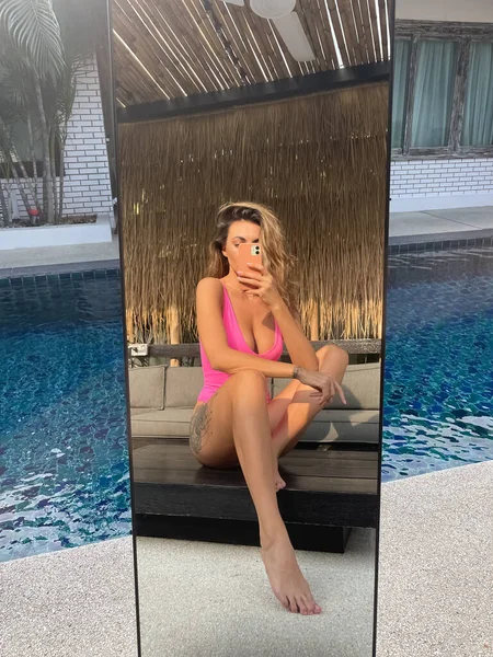 在户外 穿着亮晶晶粉色泳衣的体态丰满的晒得发亮的女人在户外的社交媒体 游泳池边垂直拍摄自己的照片 — 图库照片