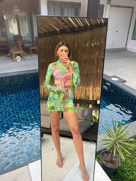 在户外 穿着绿色的短而透明的长裙 穿着运动健美的晒黑了的女人在户外的社交媒体的镜子里拍照 垂直地在游泳池边拍摄 — 图库照片