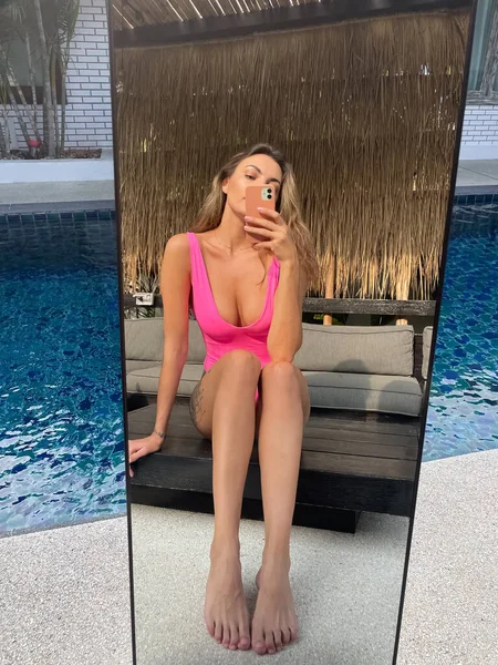 フィットスポーティな日焼けした女性で明るいピンクの水着屋外で自宅で写真を撮る上の電話で鏡の中にソーシャルメディア 垂直プールによって — ストック写真